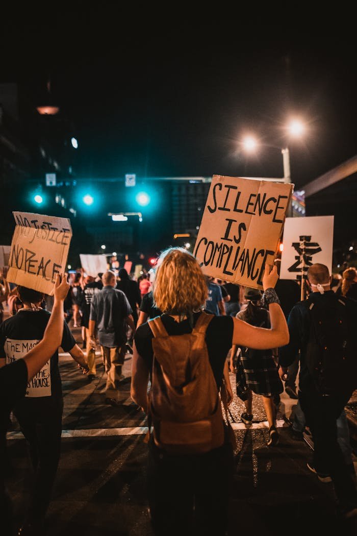 Home Activists gather at night for a protest in the city, holding signs and expressing their message.